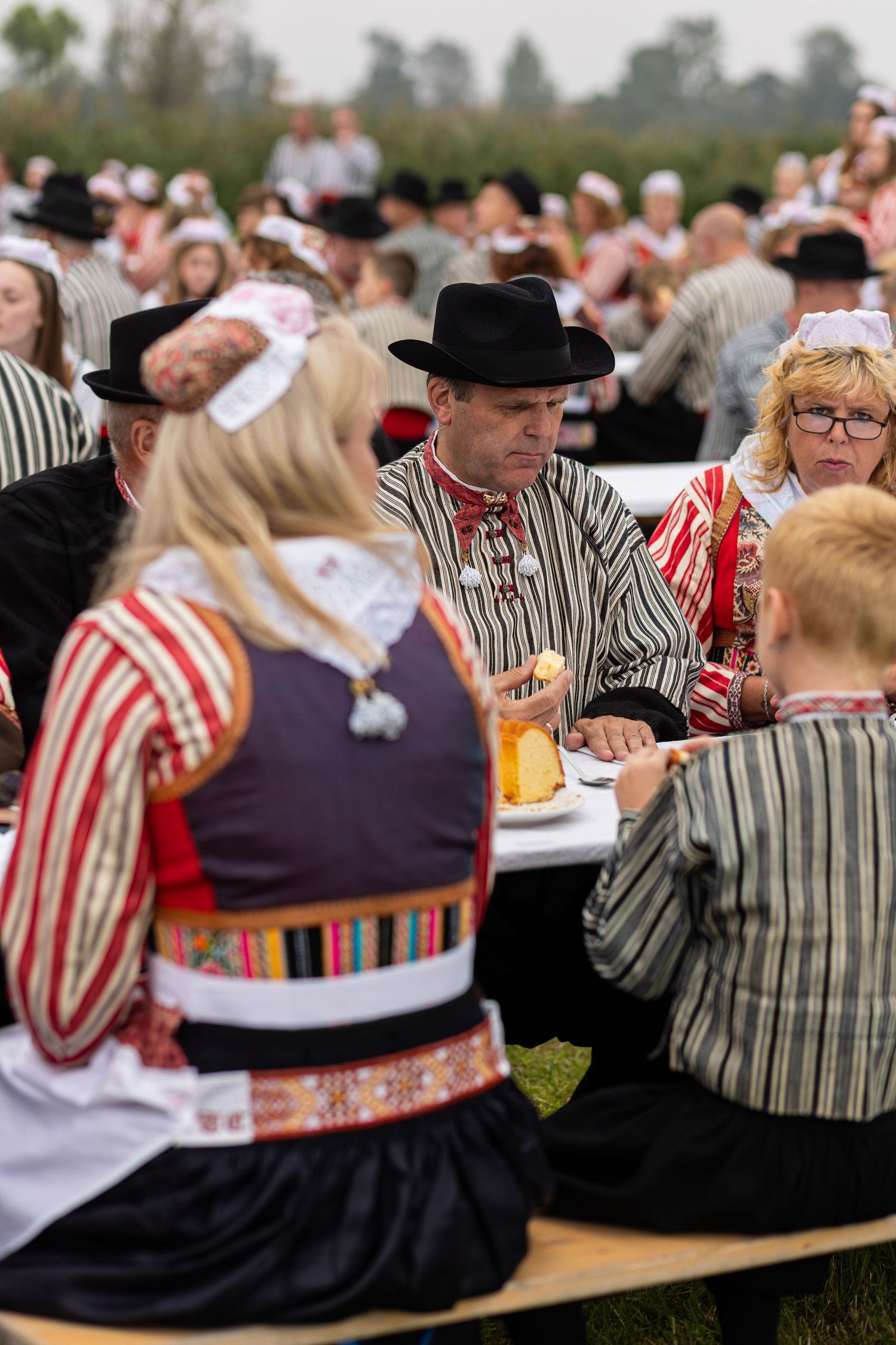 Festival attendees in traditional Dutch clothing sit at long tables during an outdoor celebration.
