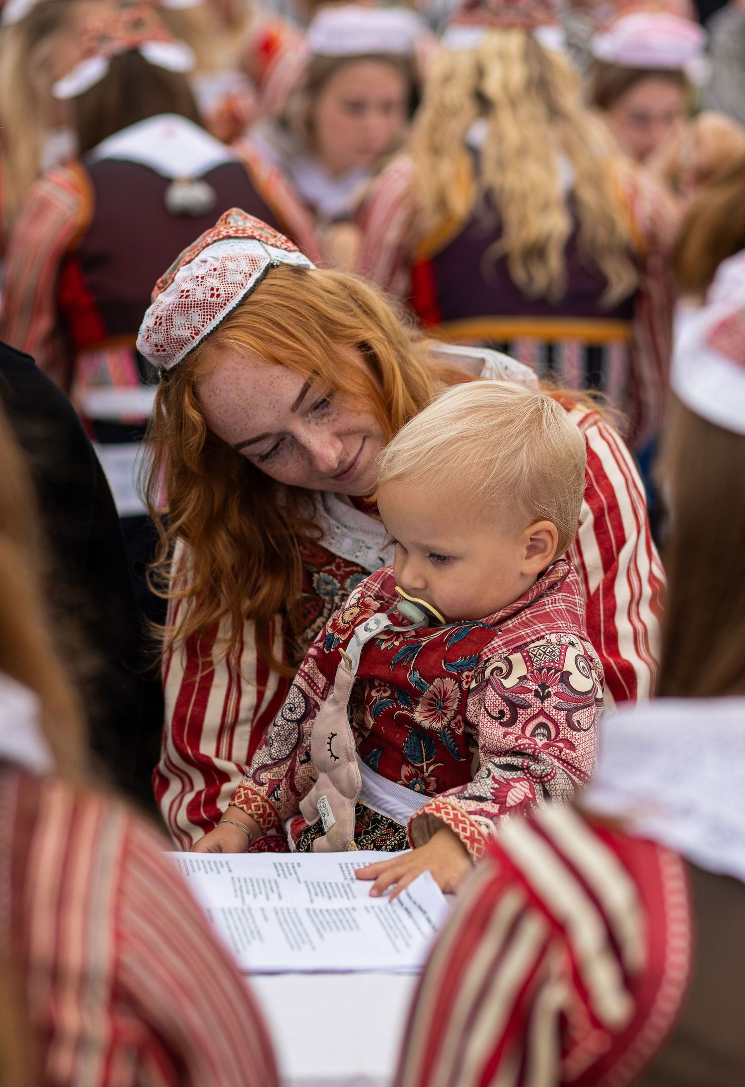 Students wearing matching red and white uniforms lean over papers at long tables during an academic gathering.