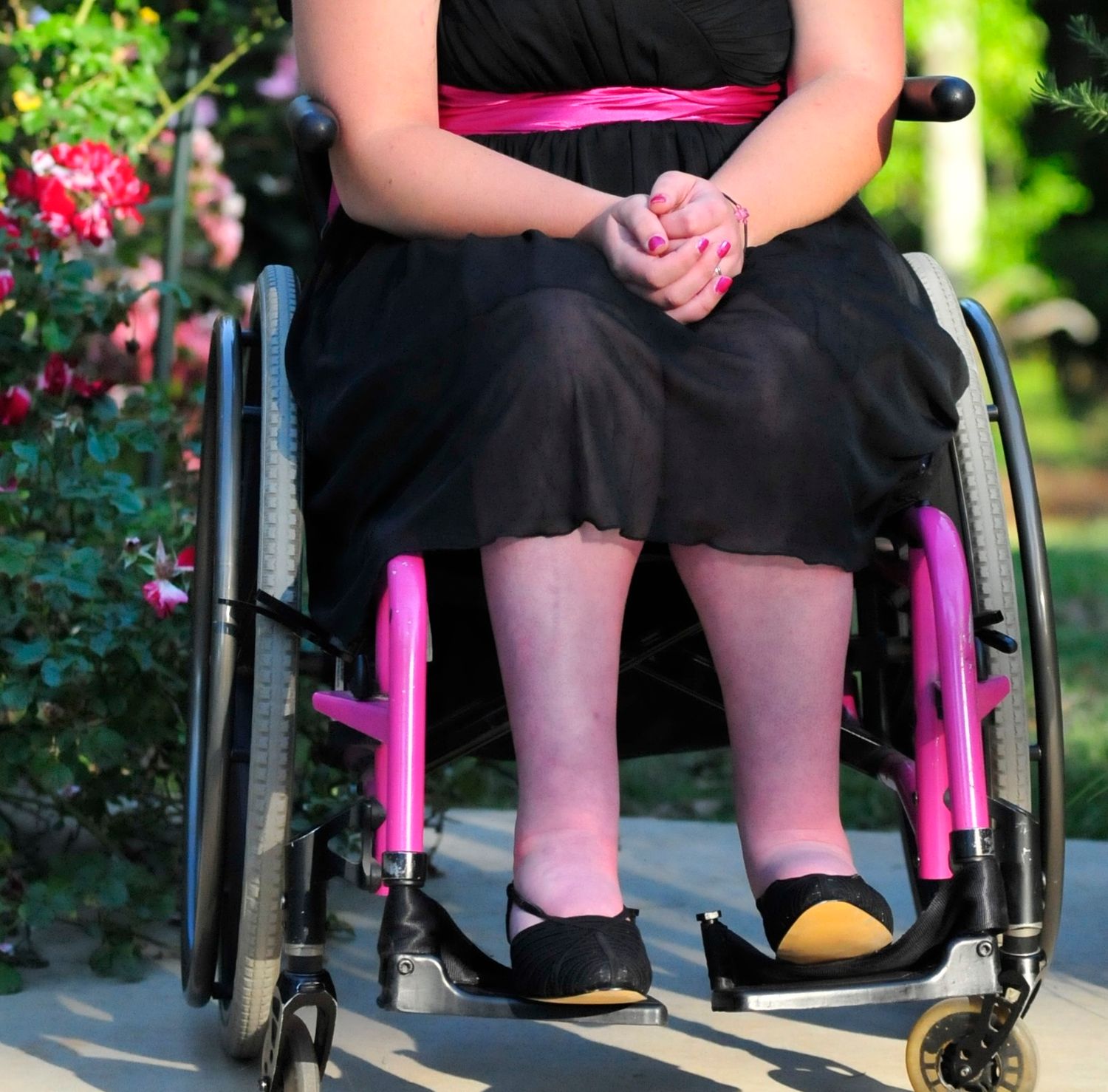 Close-up view of a wheelchair with bright pink accents and black cushioning against a blurred outdoor background.