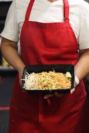 Person in red apron preparing food in commercial kitchen setting.