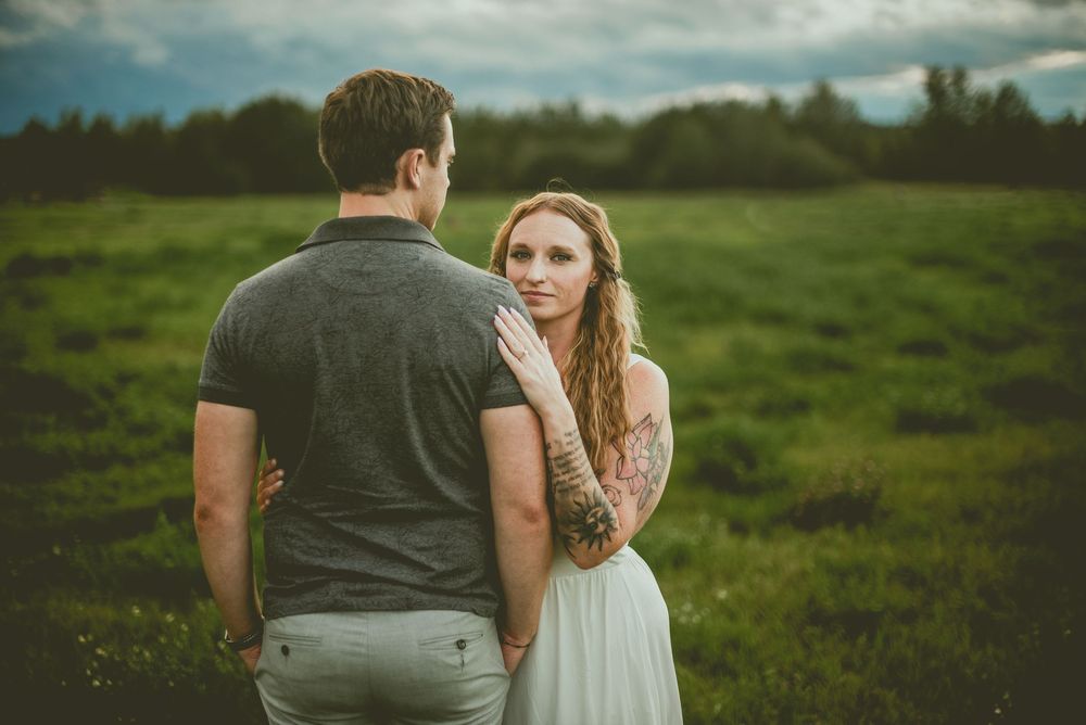 A couple shares an intimate moment together in a lush green meadow under moody cloudy skies. Edmonton Couples Photography