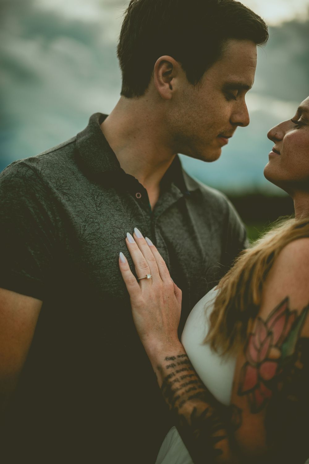 Intimate romantic couple in moody lighting with visible tattoos embrace as woman places hand on man's chest. Edmonton Couples Photography