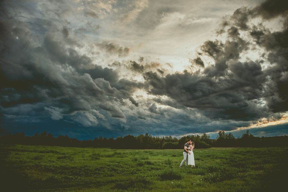 Dramatic stormy clouds hover over a lush green hillside at golden hour, creating a moody panoramic landscape Edmonton Couples Photography