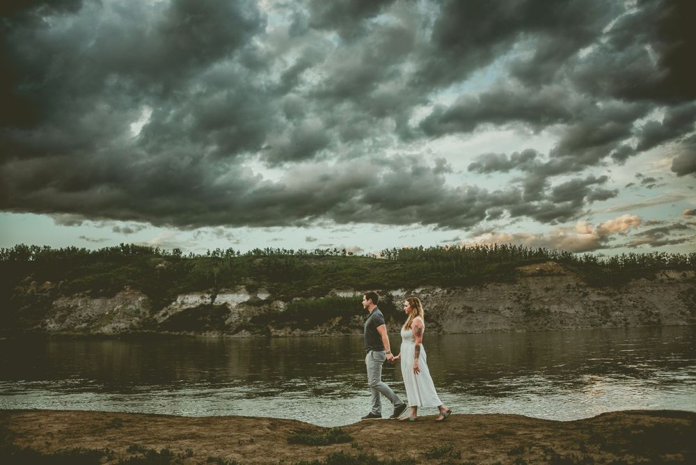 A couple stands on a dramatic shoreline under stormy clouds at sunset during a seaside wedding ceremony. Edmonton Couples Photography