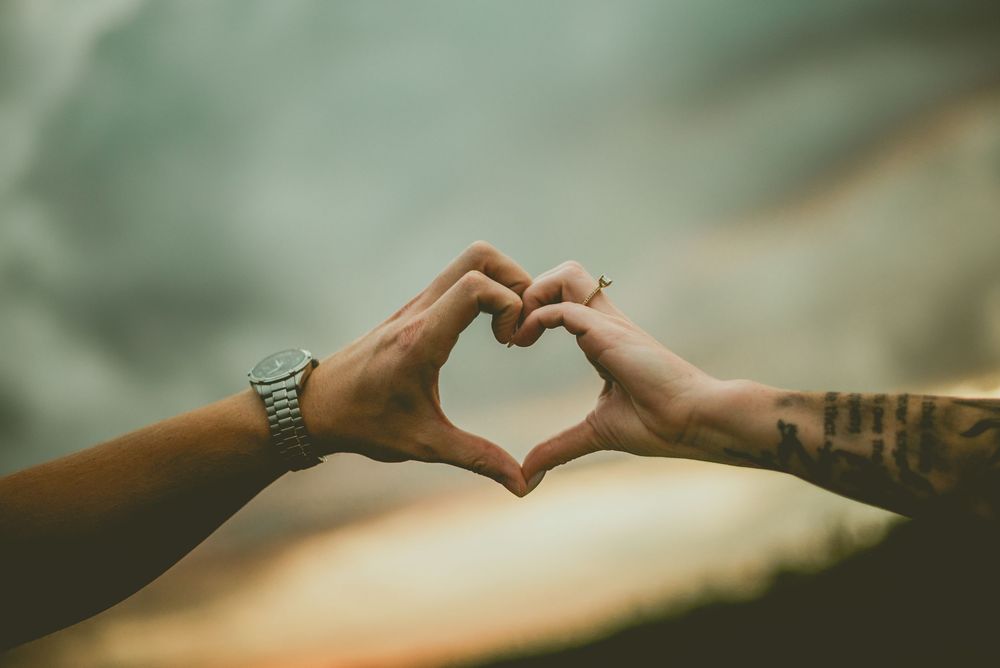 Hands come together to form a heart shape silhouetted against a blurred natural background. Edmonton Couples Photography