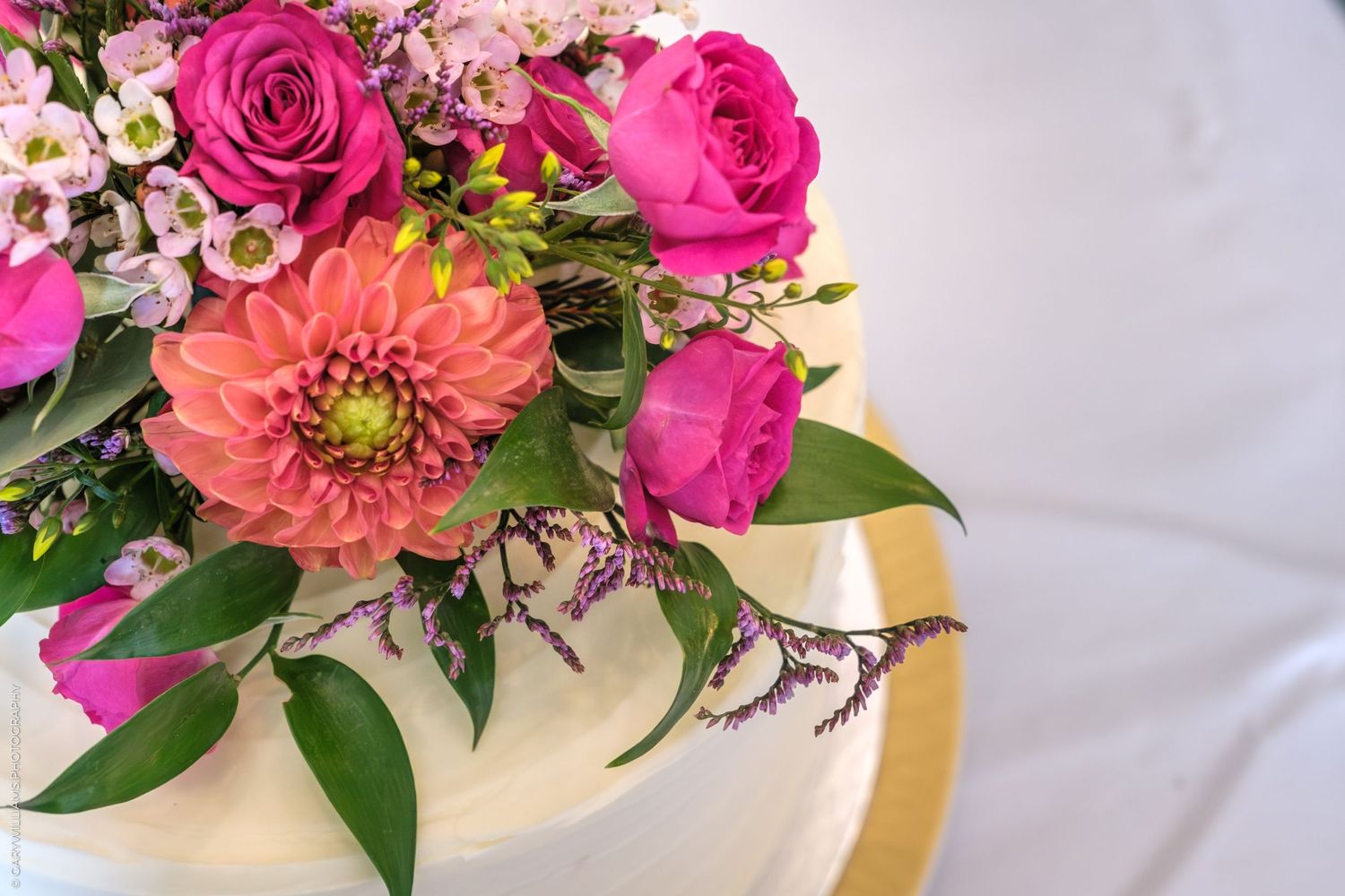 Pink roses and coral dahlias arranged with delicate foliage in an elegant centerpiece on white table linens.