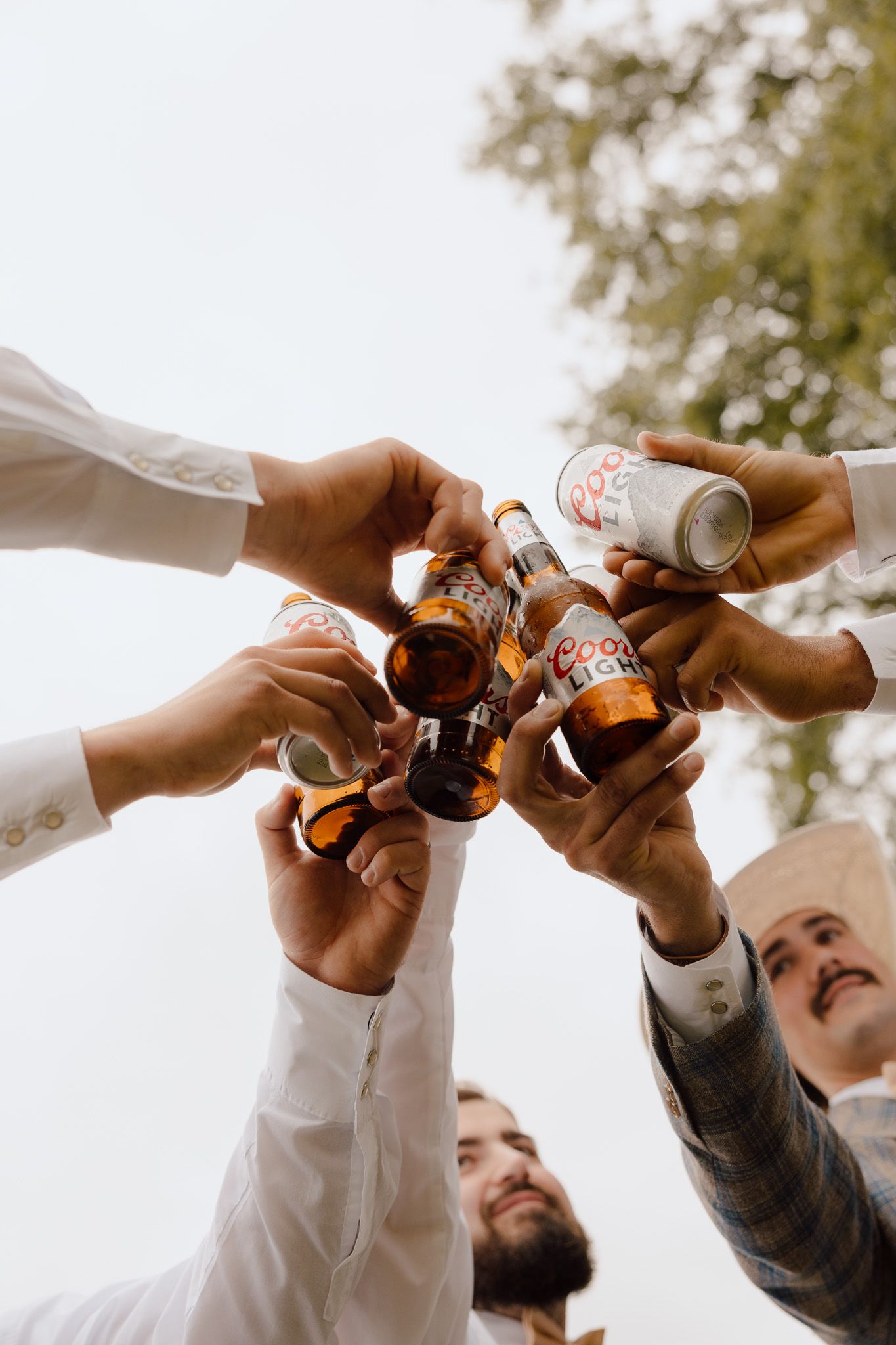 Groomsmen toasting with Coors Light beer bottles and cans outdoors at a wedding celebration.