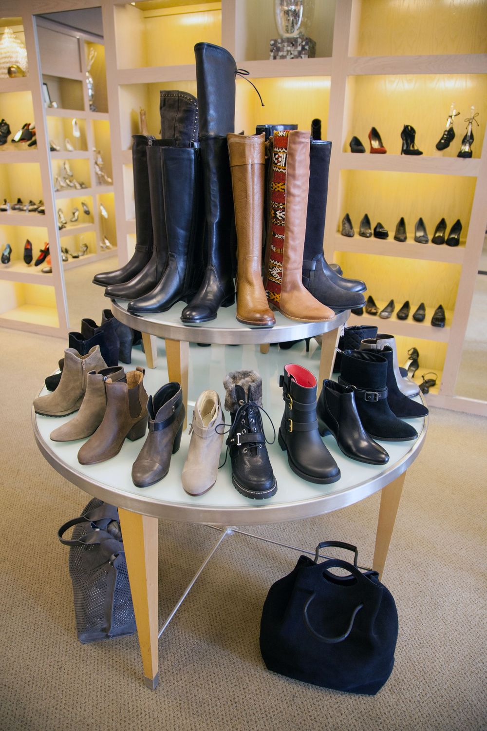 Various leather boots and shoes displayed on curved white retail shelving units against a yellow wall in a shoe store.