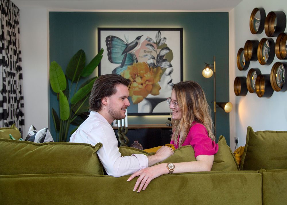 Two people lounge on an olive green couch and share an intimate conversation in a modern living room.