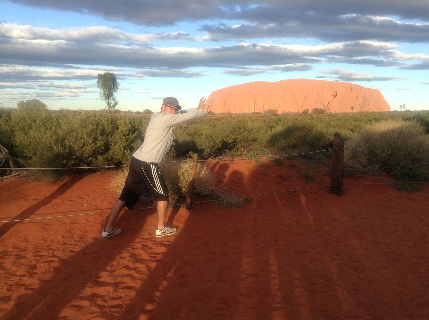 Panoramic view shows a group of people hiking across a vast desert landscape with rugged terrain and sparse vegetation.
