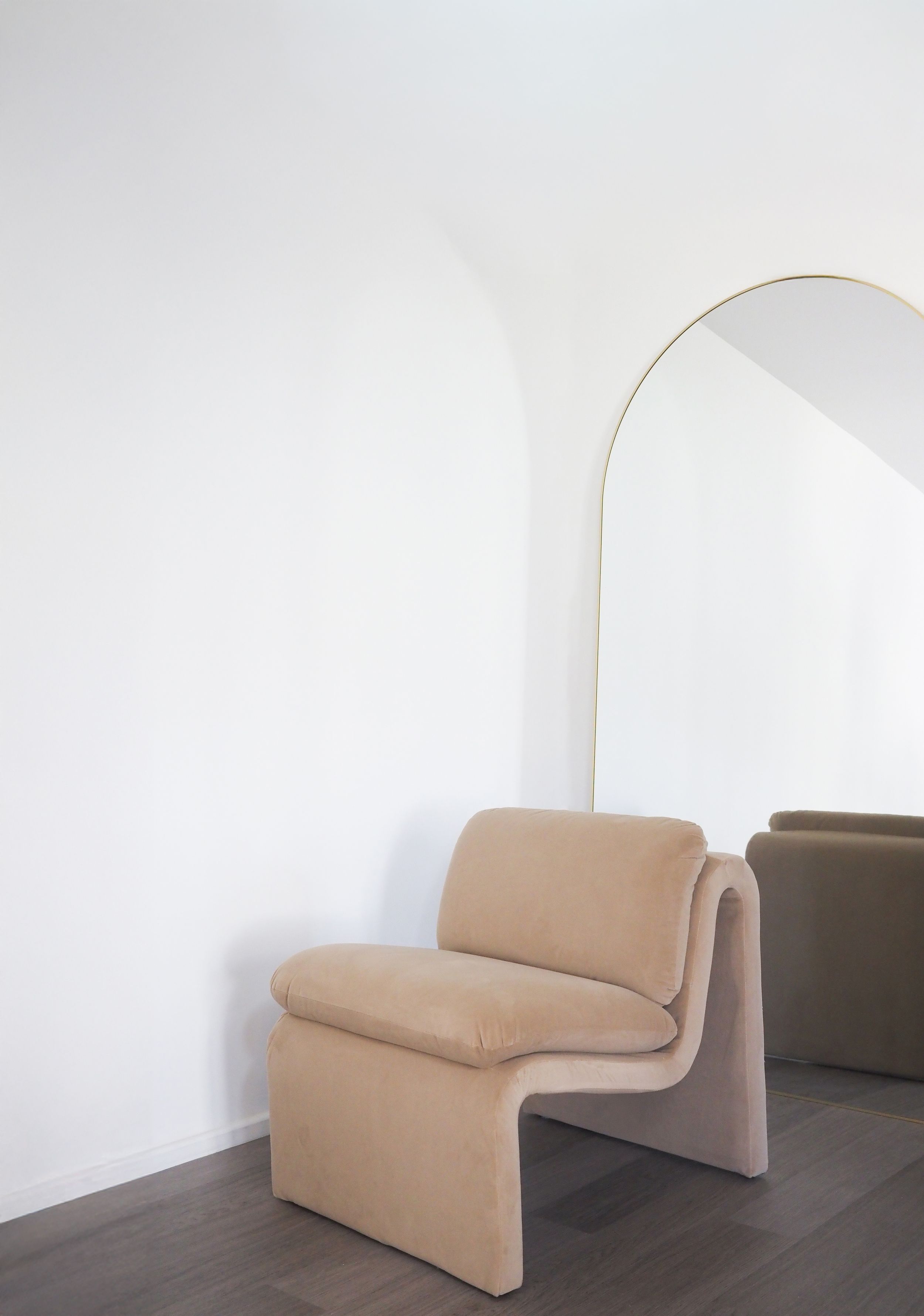Modern beige upholstered curved accent chair with minimalist design against white wall in contemporary space.