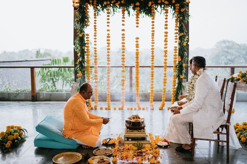 Wedding ceremony setup with floral decorations and hanging orange garlands in an outdoor venue overlooking mountains.