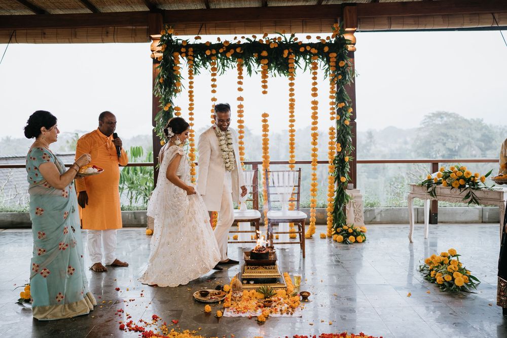 Wedding guests gather around a decorated ceremony space with orange floral garlands and mountain views.