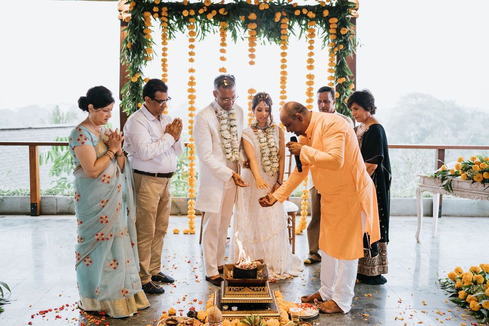 Wedding guests participate in traditional ceremonies under orange marigold garlands in an outdoor venue.