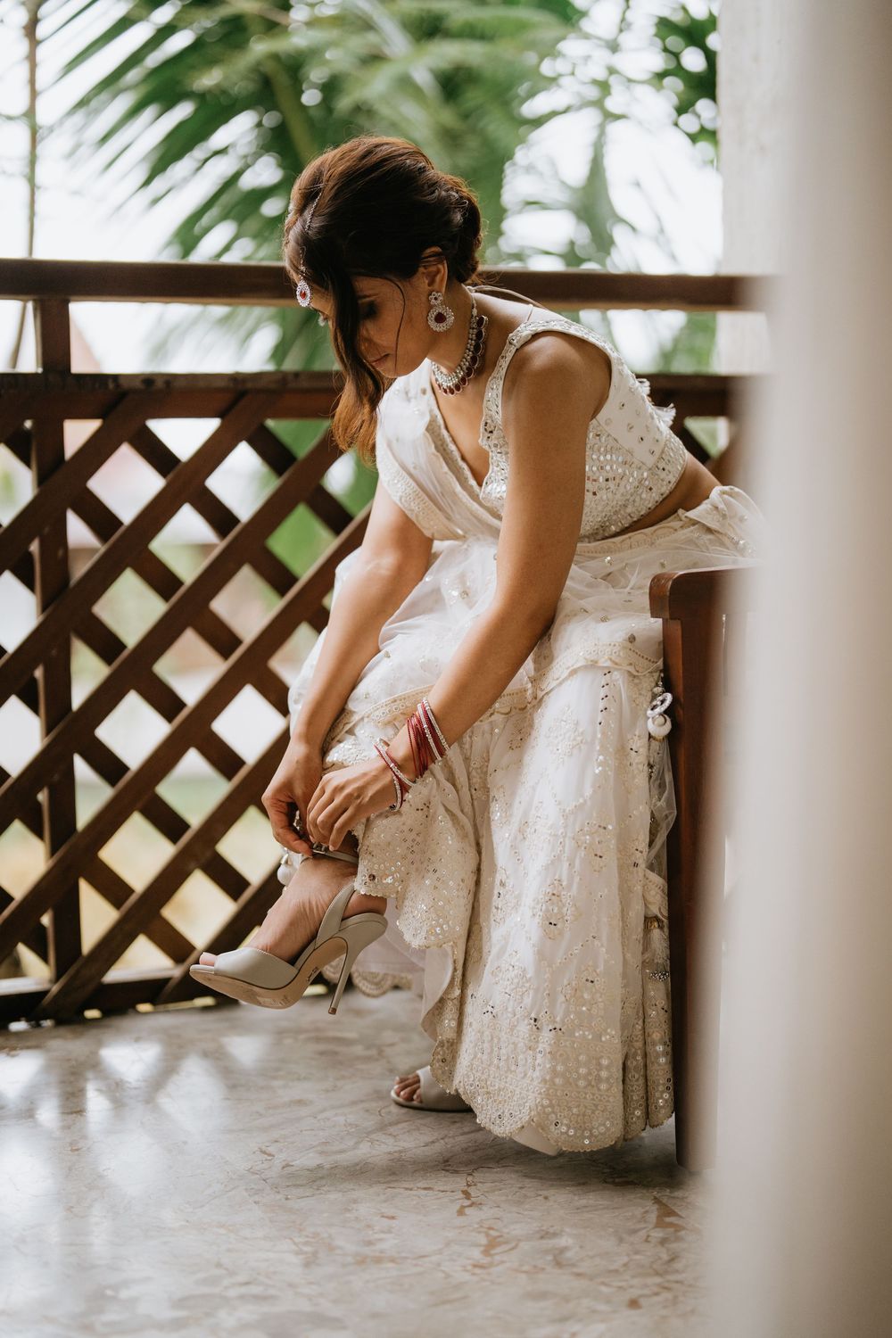 Close-up shots of a bride adjusting her shoes on a porch with lattice details and tropical plants.