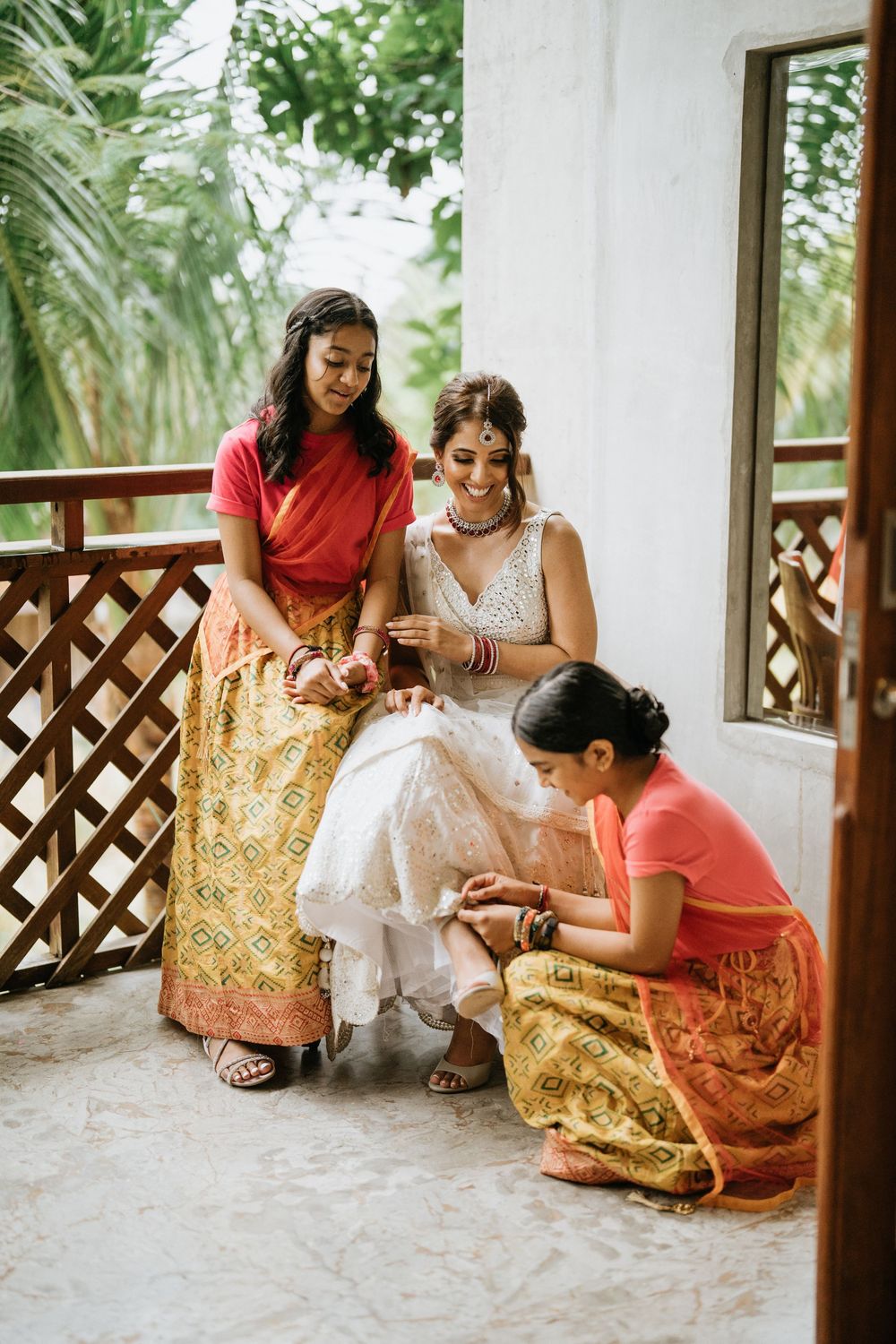 Wedding preparations showing attendants helping with final dress adjustments on a covered porch.