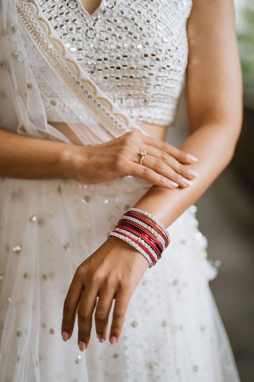 Close-up details of traditional Indian wedding bangles and jewelry against a white lace dress.