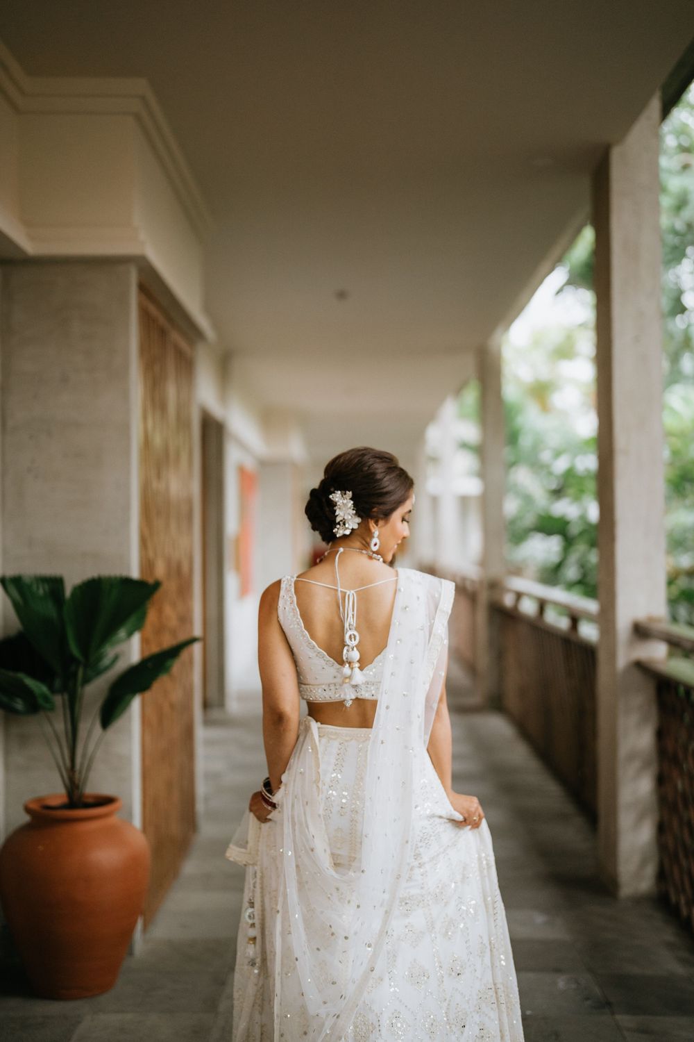 A flowing white lace wedding dress captured in movement along a covered walkway with terracotta planters.