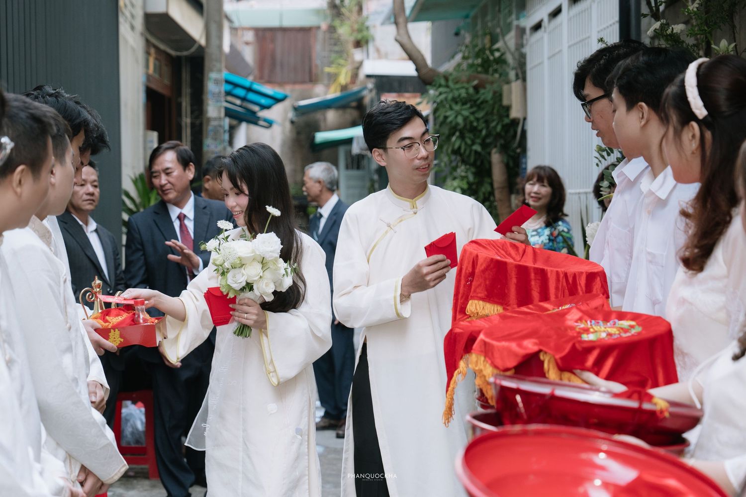 Vietnamese traditional wedding ceremony with guests in ao dai carrying red lacquer trays.