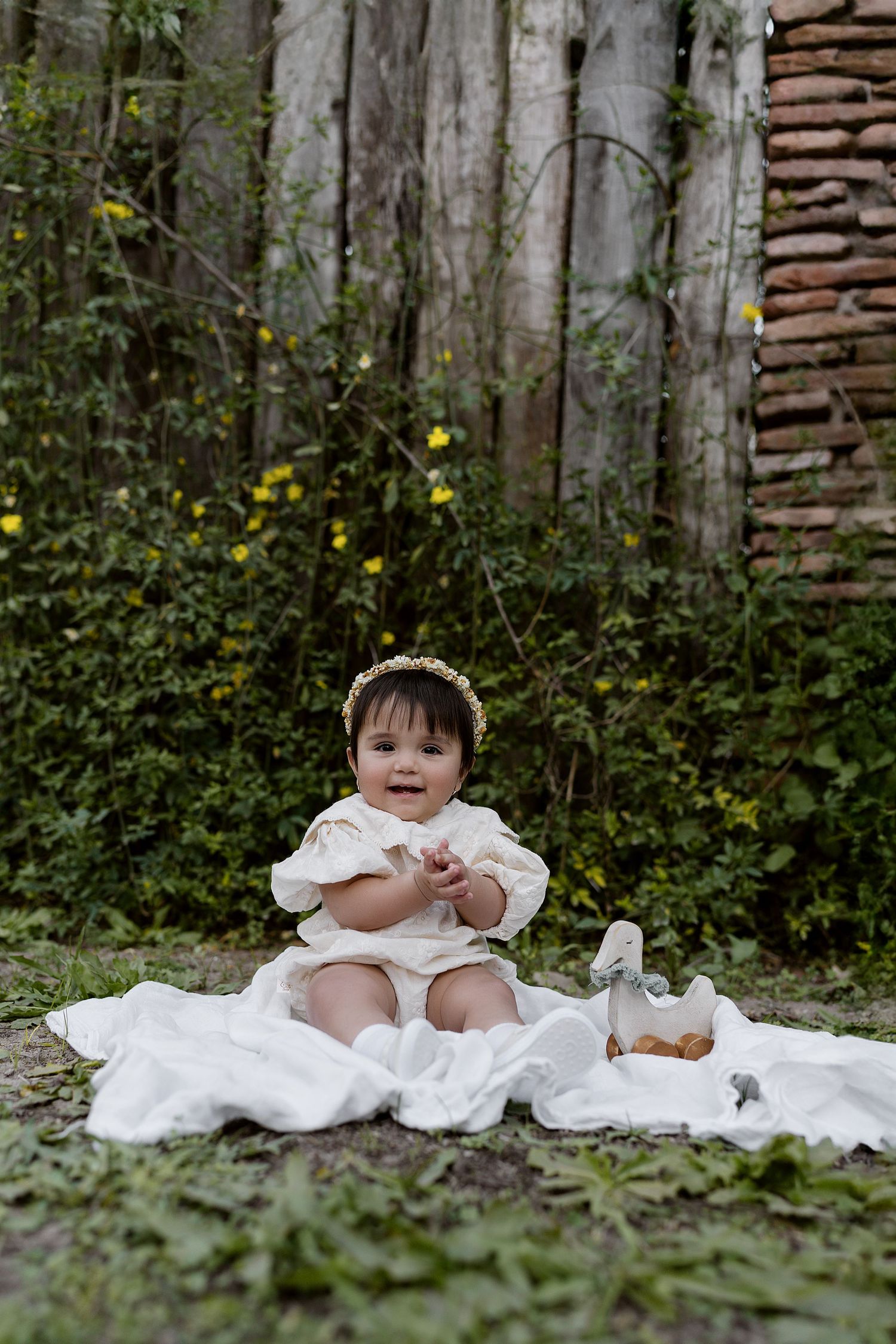 A series of charming photographs showing a child in a flowing white dress sitting against a rustic wooden fence outdoors.