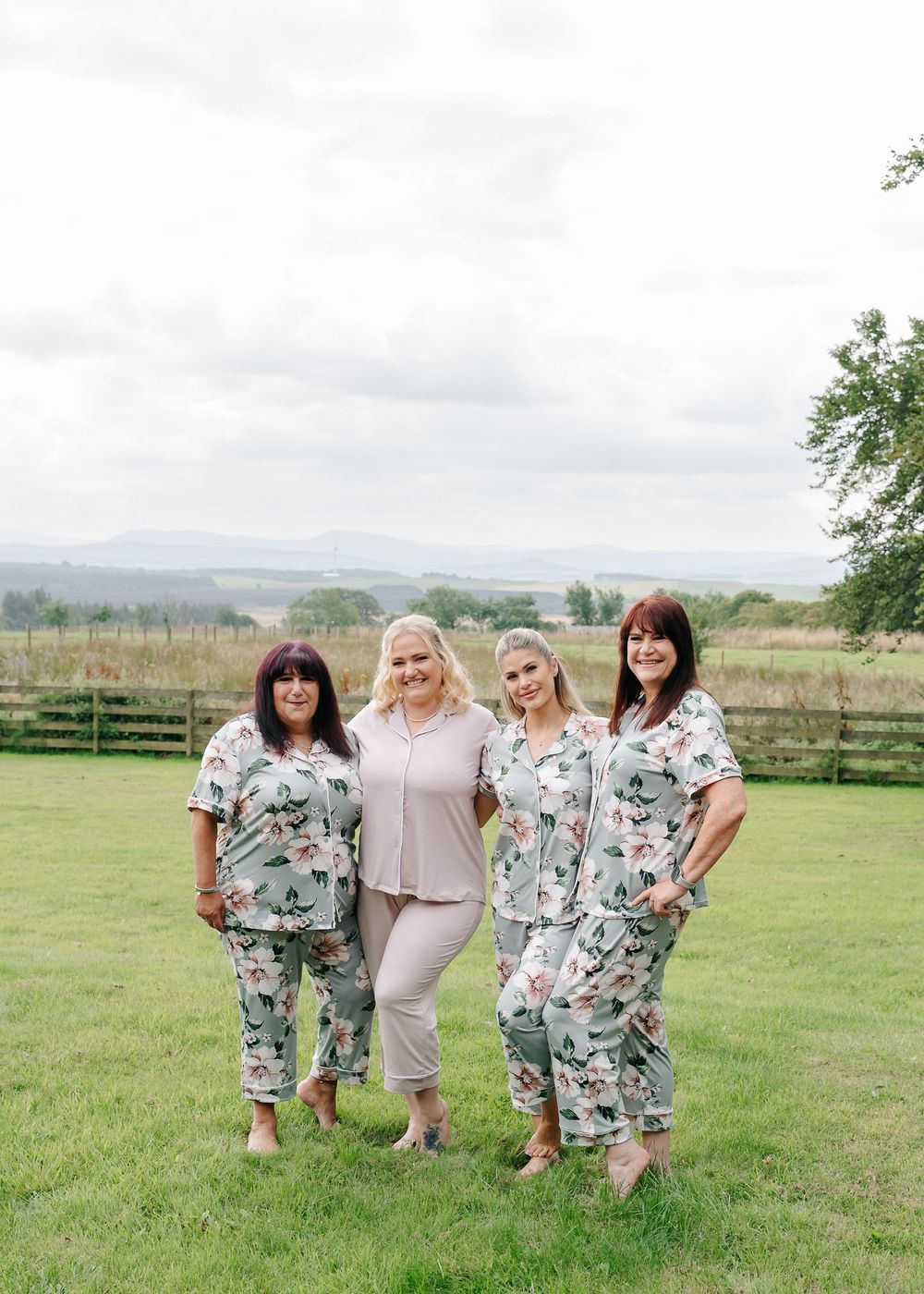 Group photo in a rural field showing people wearing coordinating floral dresses and solid pastels.