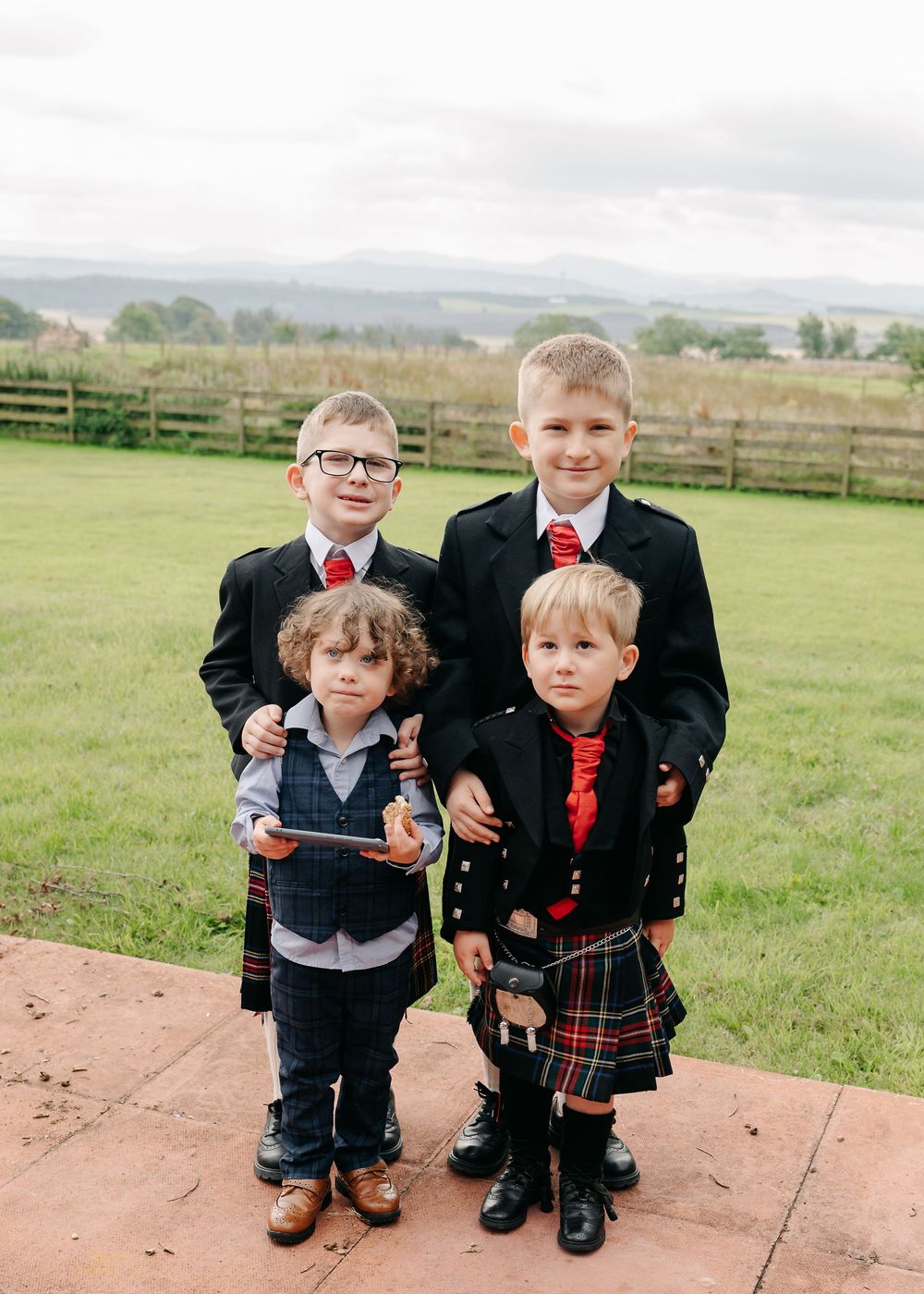 Young children dressed in formal Scottish attire pose together on outdoor stone steps.