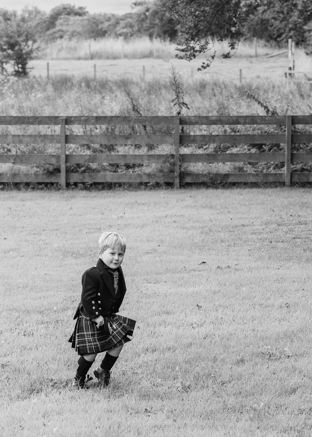 Black and white sequence shows children in formal attire playing in a grassy field.