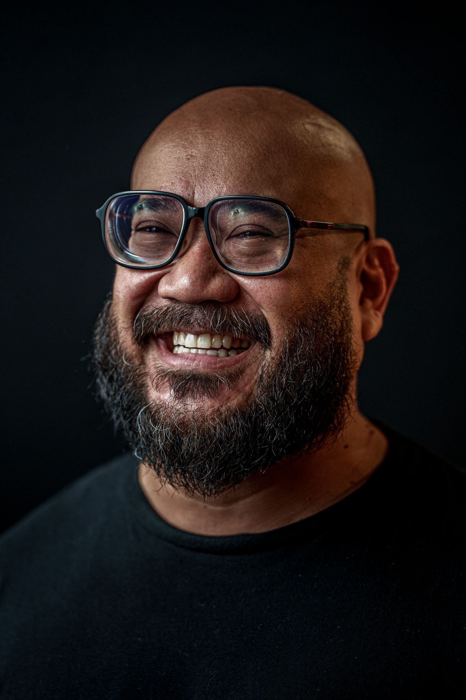 Professional portrait series on dark background showing expressive close-up shots with glasses and full beard.