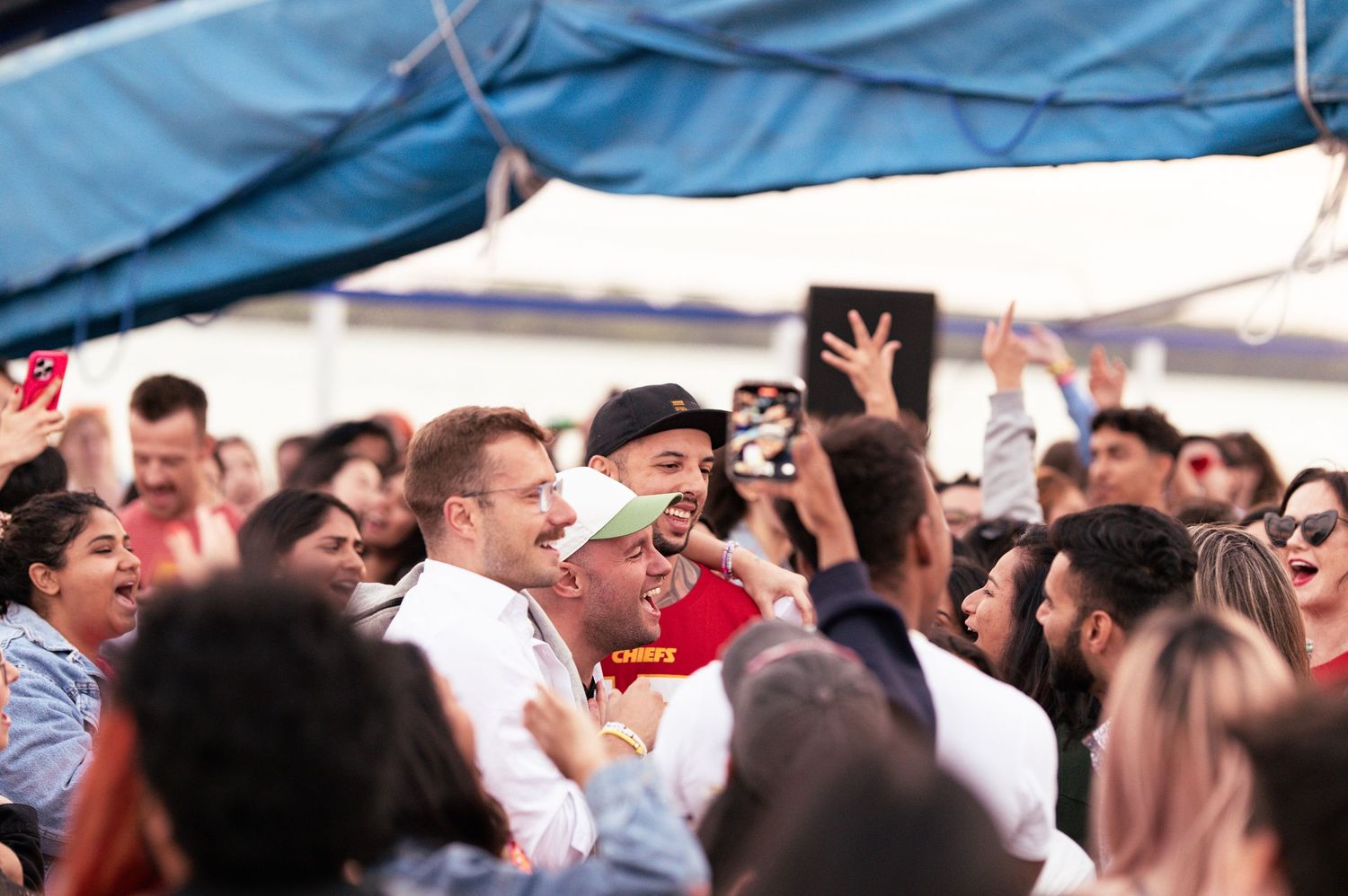 Excited crowd of sports fans gather under a tent during a celebratory moment.