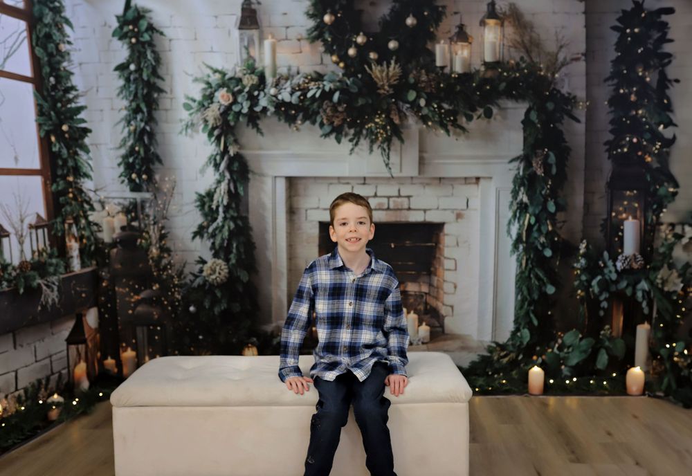 Young person in plaid shirt standing in front of decorated Christmas fireplace setting.