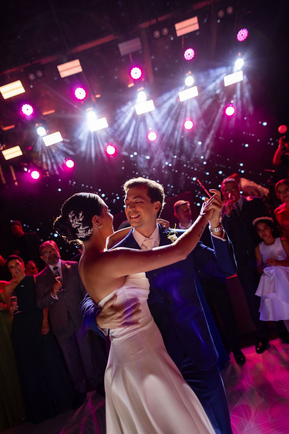 Couples dance together on a wedding reception dance floor illuminated by purple and white stage lights.