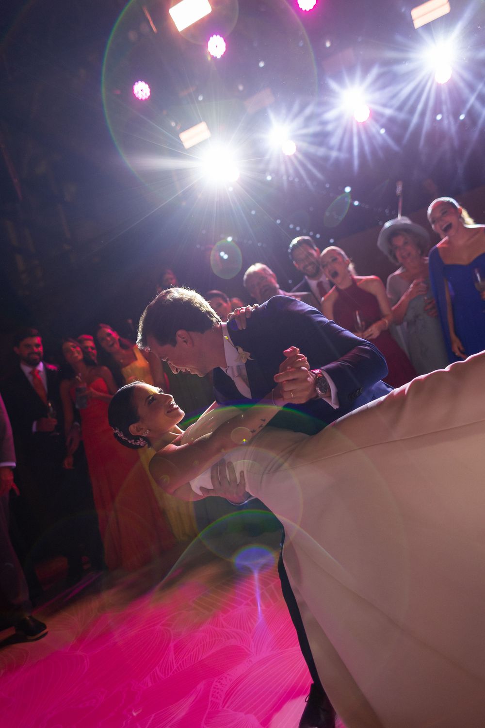 Wedding reception dance floor with bright spotlights creating dramatic silhouettes of dancing guests.