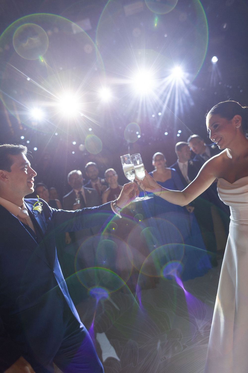 Wedding guests dance under bright theatrical lighting at an elegant reception venue.