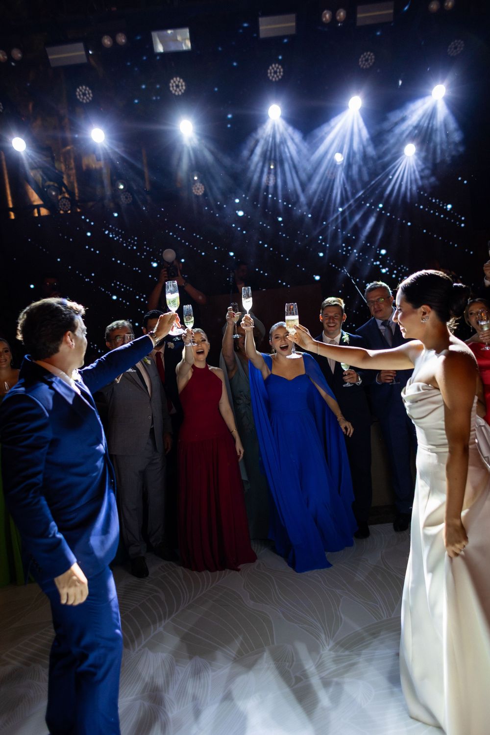 Wedding guests form a circle on the dance floor under dramatic blue and white spotlights.