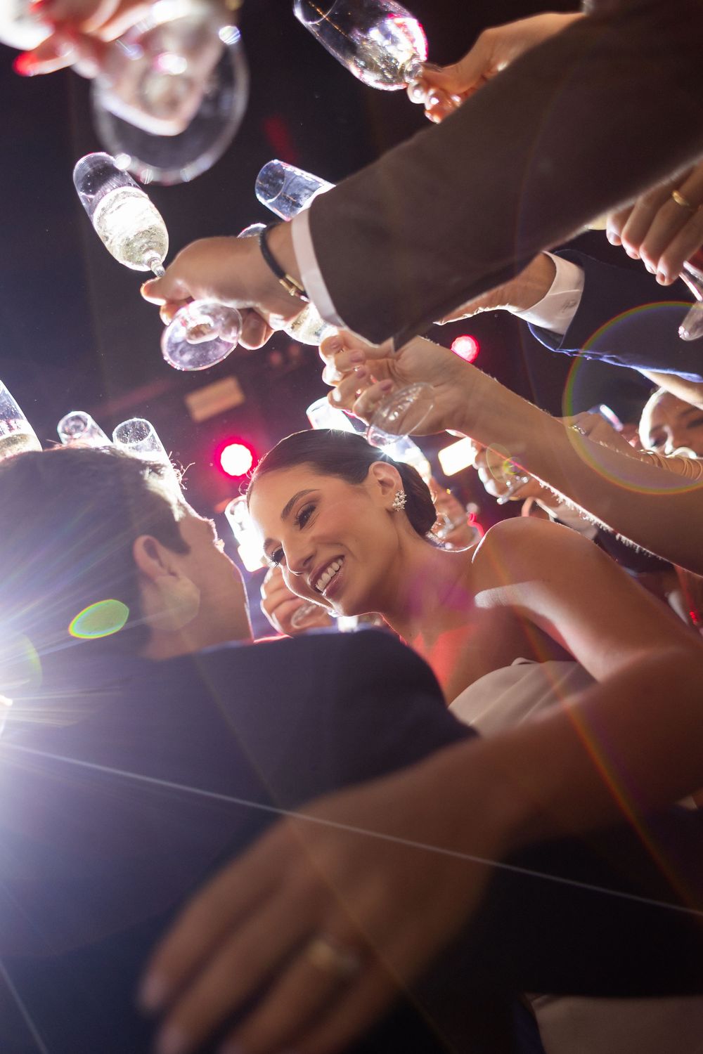 Celebratory champagne glasses raised in a toast with light flares and joyful expressions at an evening party.