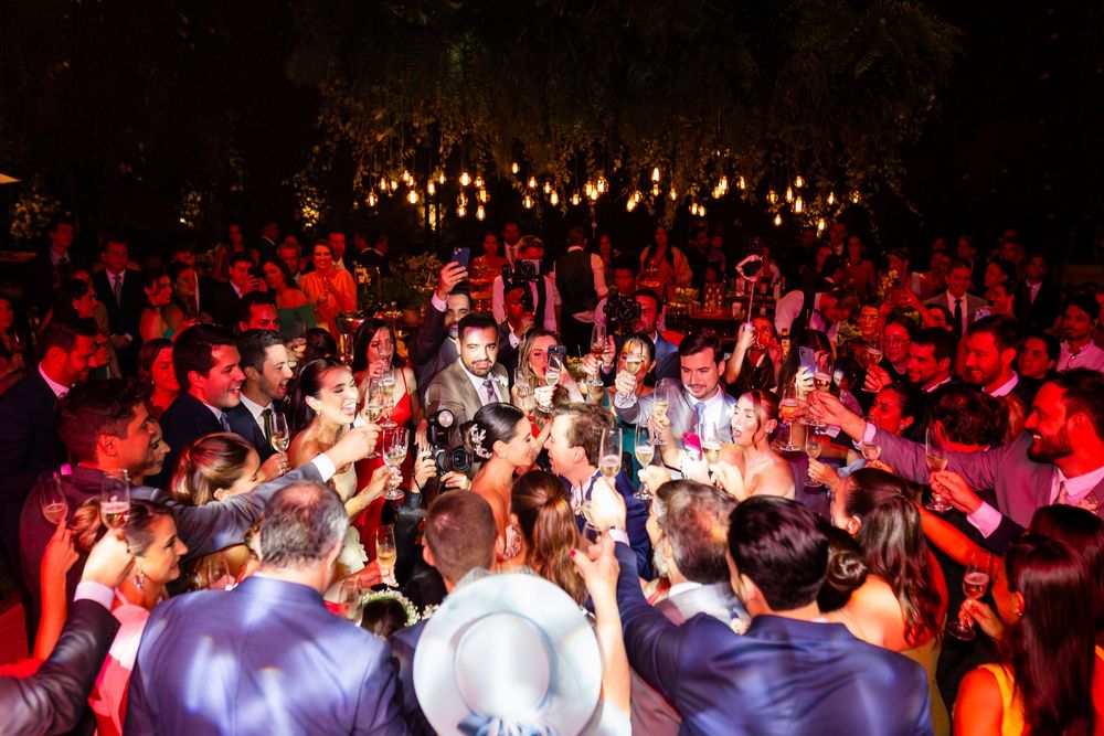 Large crowd of people dancing and celebrating at a dimly lit indoor event venue with red lighting.