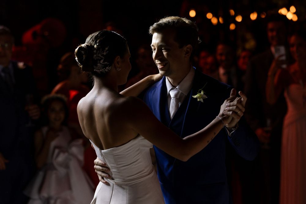 Couple sharing an intimate dance during wedding reception under dramatic lighting and among crowd.