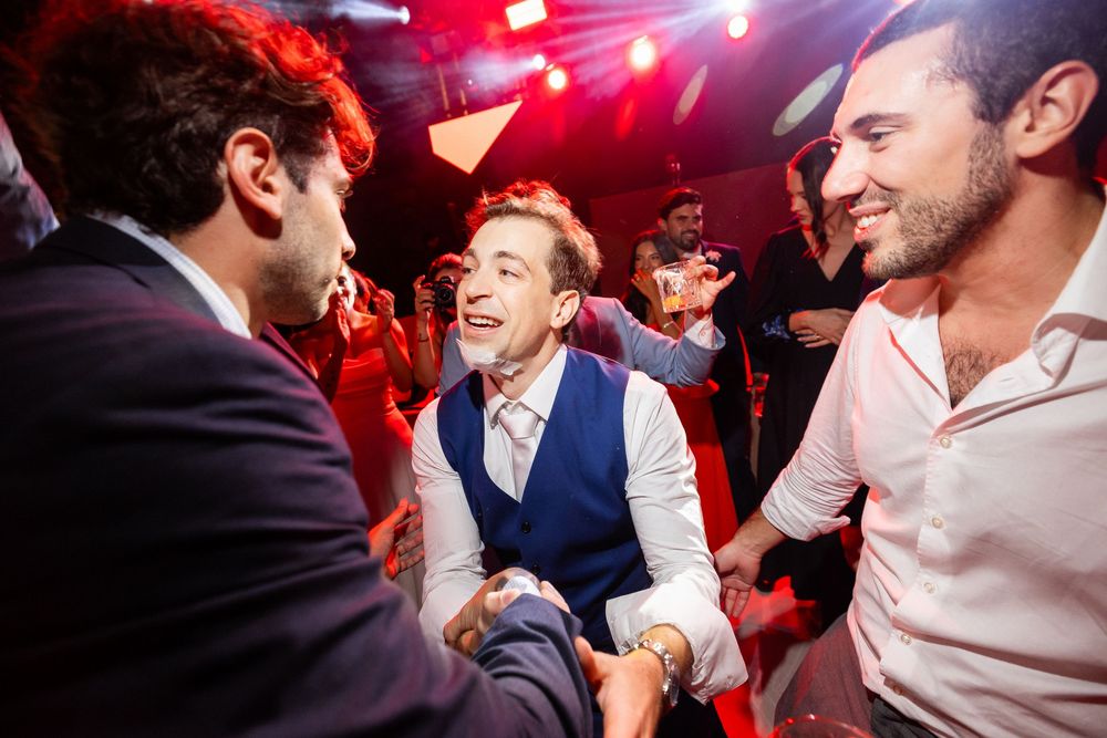 A lively wedding reception dance floor scene with people celebrating under red lighting.