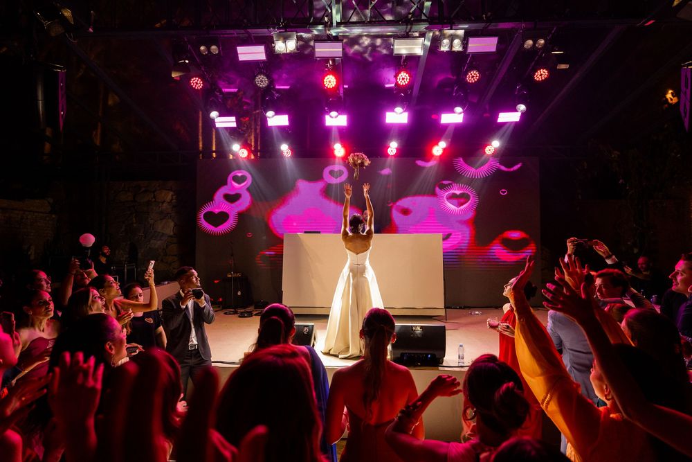 Concert crowd raising their hands in a dark venue illuminated by vibrant purple stage lights.