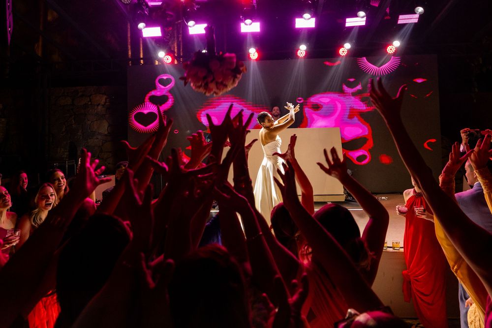 Dark concert venue with dramatic pink and purple lighting casting shadows over the energetic audience.