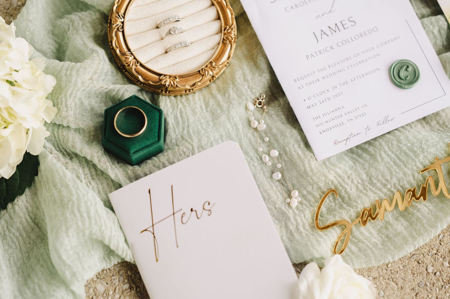 Wedding invitation suite displayed on sage green linen with gold details, white paper and emerald green wax seals.