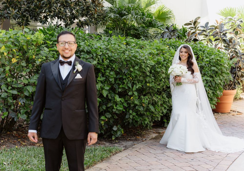 Wedding couple and wedding party members pose outdoors in garden setting with lush greenery backdrop.