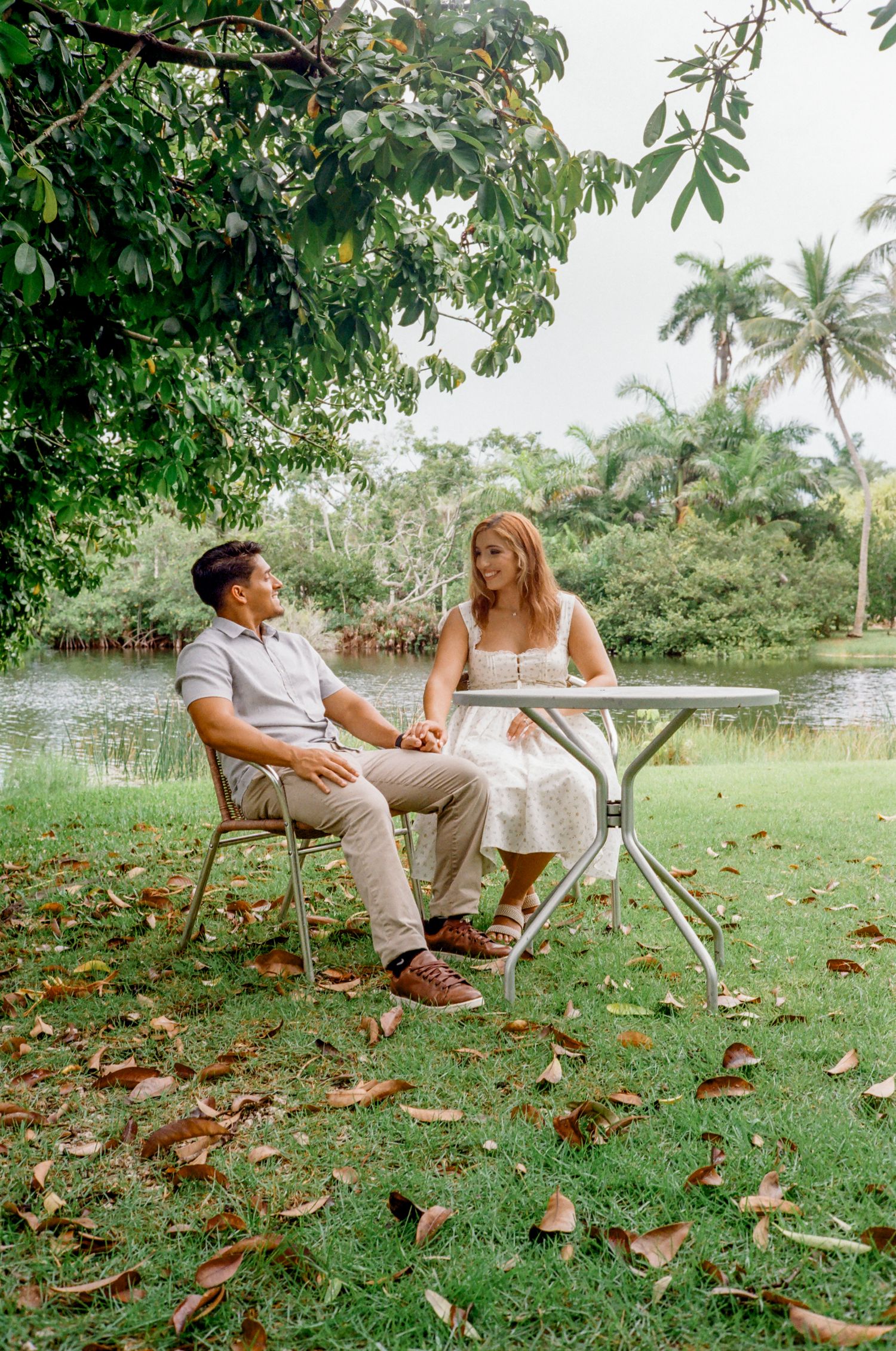 Two people relaxing on chairs outdoors at a scenic table setting surrounded by lush green grass and fallen leaves.