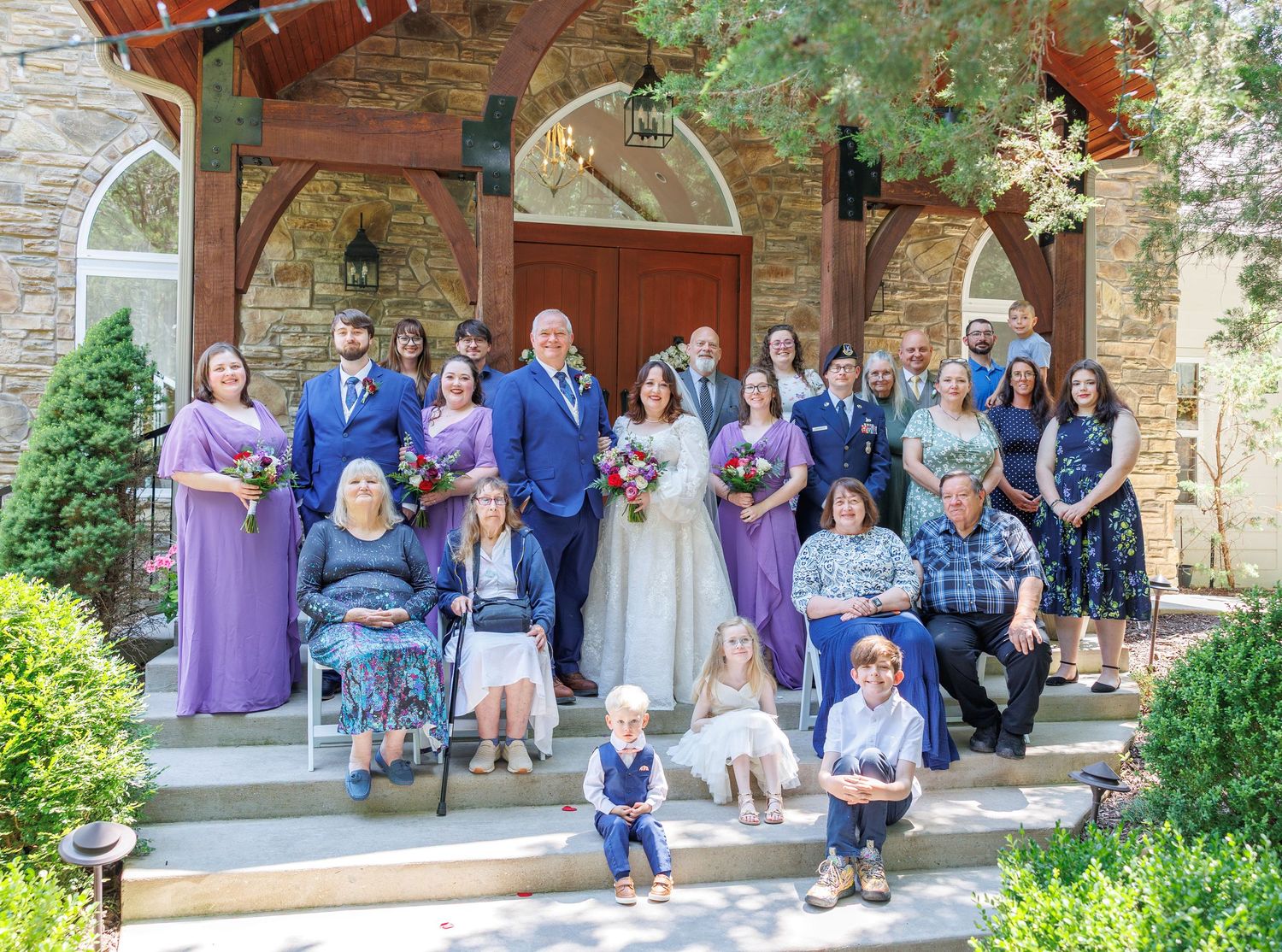 Wedding party group poses together on brick church steps in coordinated blue and purple attire at Dooley's Chapel in Branson, MO.