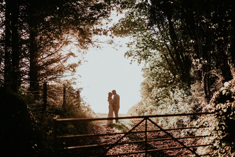 Silhouetted couple standing on wooden bridge in misty forest during golden sunset.