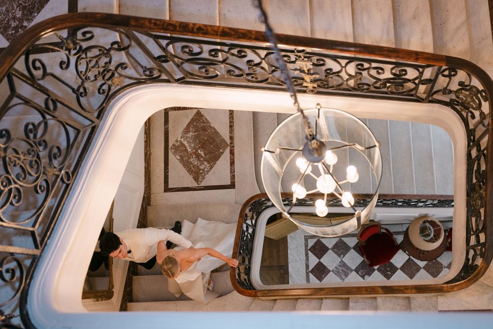 Elegant staircase with ornate wrought iron railing and modern spherical chandelier viewed from above in luxury interior.