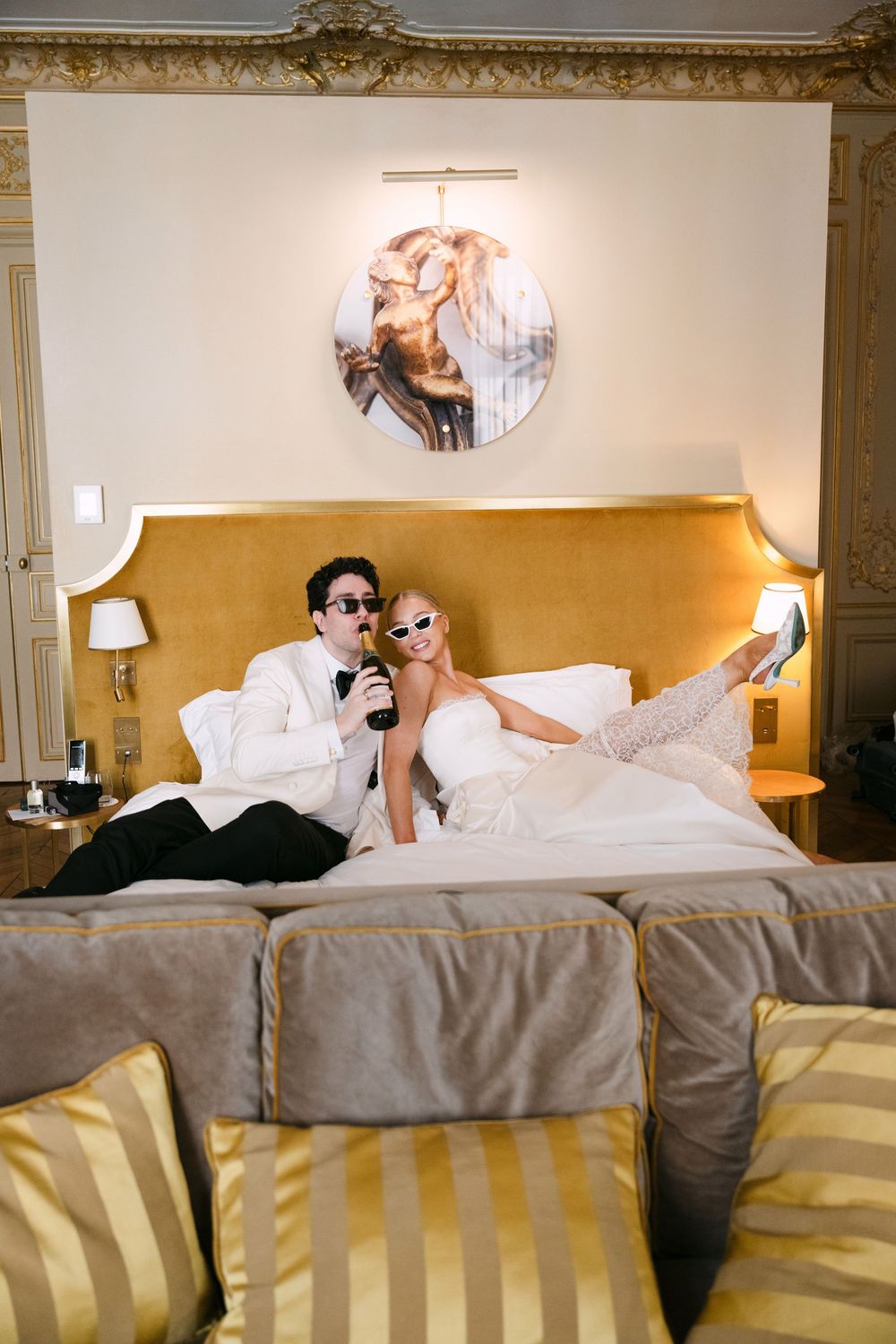 A couple in sunglasses lies on a hotel bed in a playful pose for a series of connected photos.