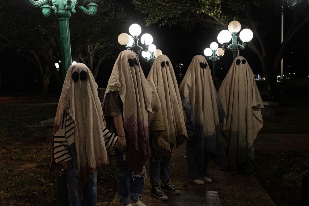 Ghost costumes gathered under vintage street lamps at night creating an eerie scene.