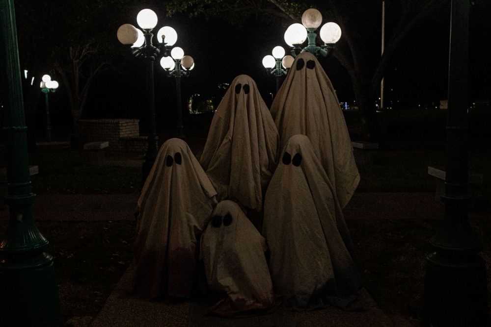 White sheet ghost decorations stand in a row against a dark background with glowing lights.