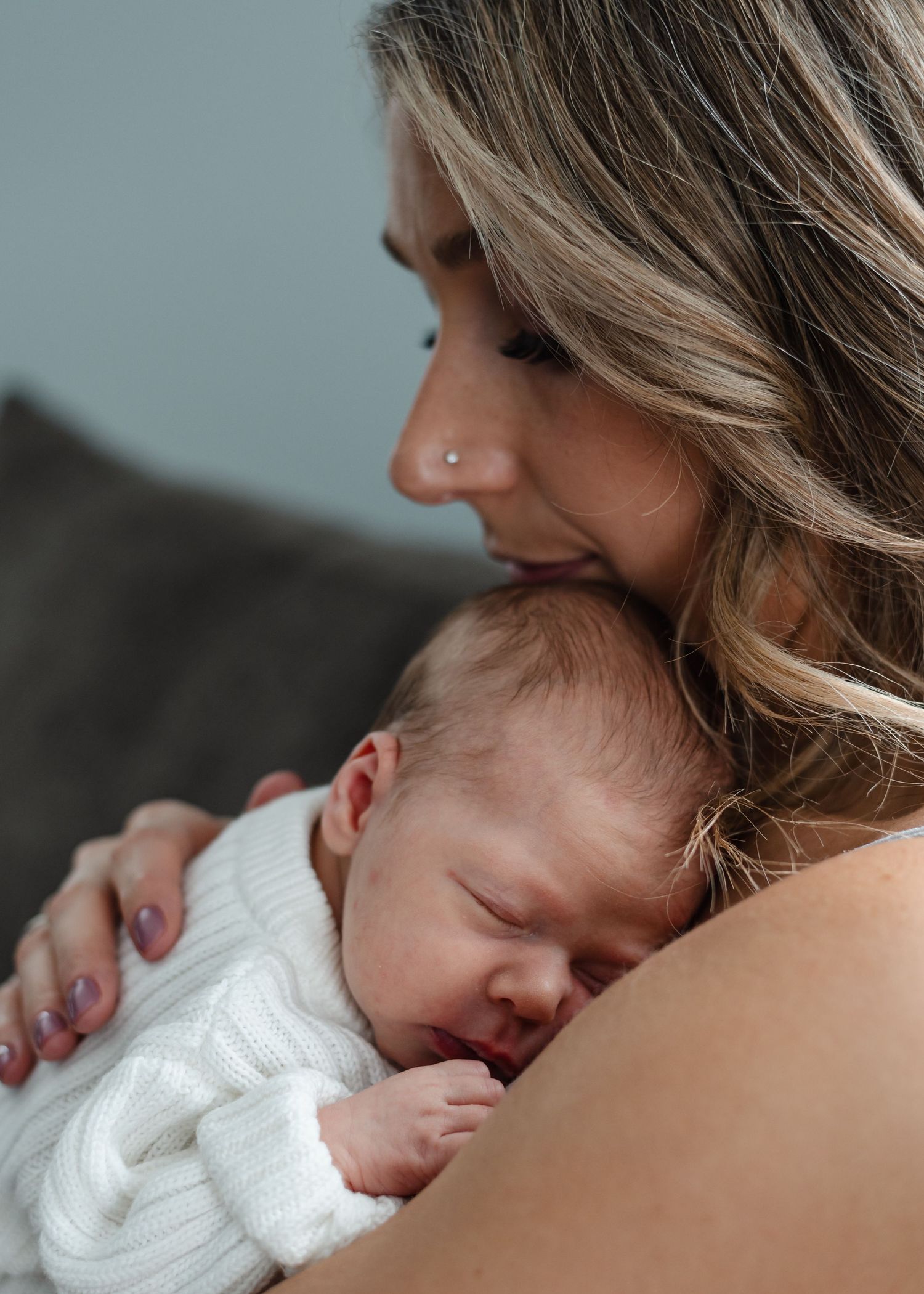 Mother holding and comforting newborn baby in soft lighting with tender skin-to-skin contact.